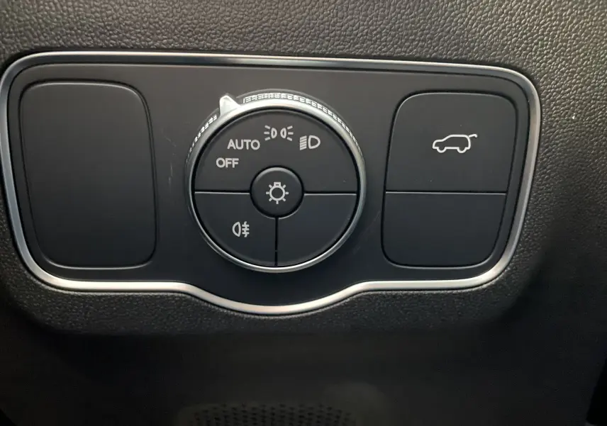 Gros plan sur le bouton de commande des phares et l'ouverture du coffre dans l'habitacle noir du JAECOO J5 Phantom Grey 2026.