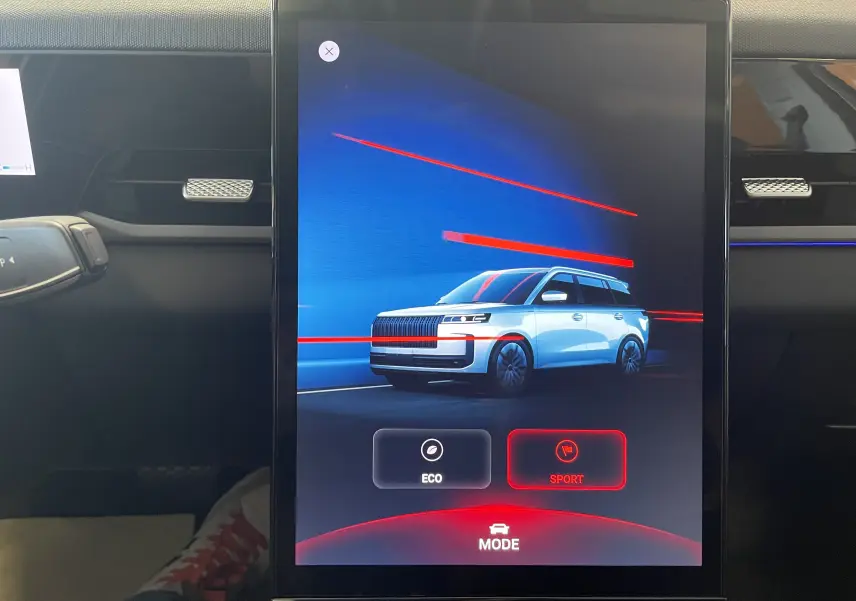 Écran tactile intérieur montrant la JAECOO J5 grise en 3/4 avant avec options de mode Eco et Sport.