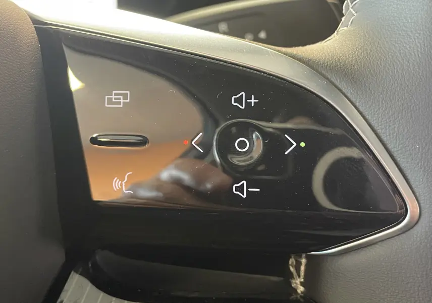 Gros plan sur les commandes de volume et de navigation multimédia sur le volant en cuir noir du JAECOO J5 Phantom Grey.