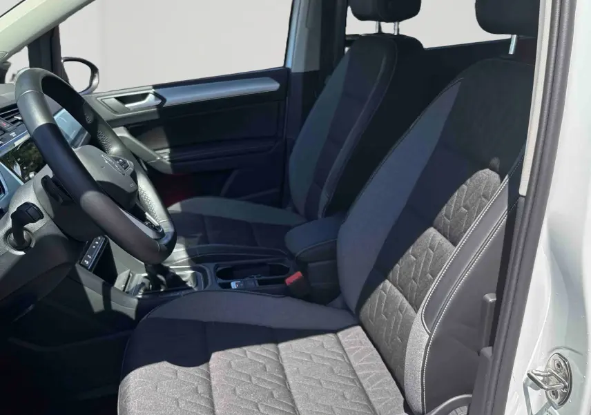 Vue intérieure côté conducteur du Volkswagen Touran 2025 avec sièges tissu gris et volant multifonctions en cuir.