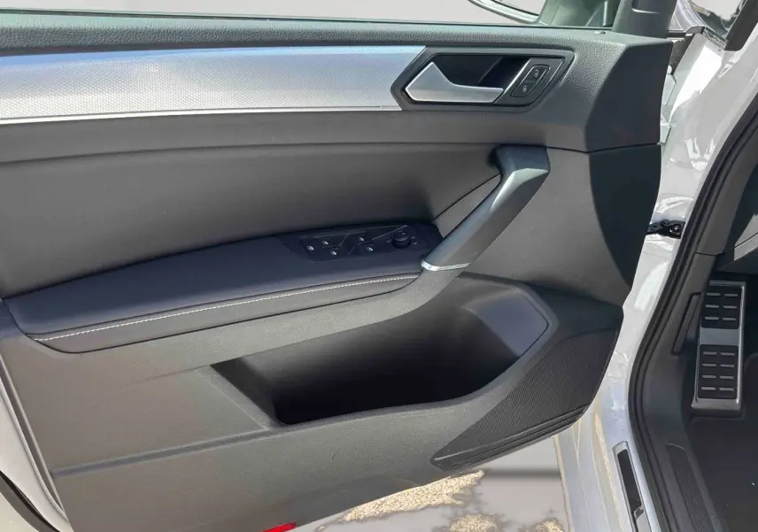 Vue intérieure de la porte avant gauche du Volkswagen Touran blanc, avec commandes de vitres et poignée argentée.