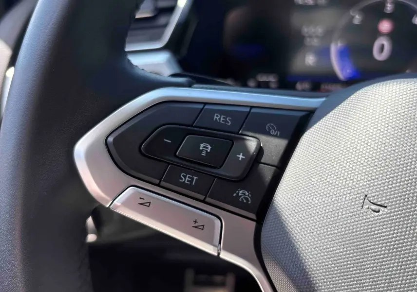 Gros plan sur les commandes du volant cuir multifonctions du Volkswagen Touran blanc, avec régulateur adaptatif et assistant de maintien de voie.