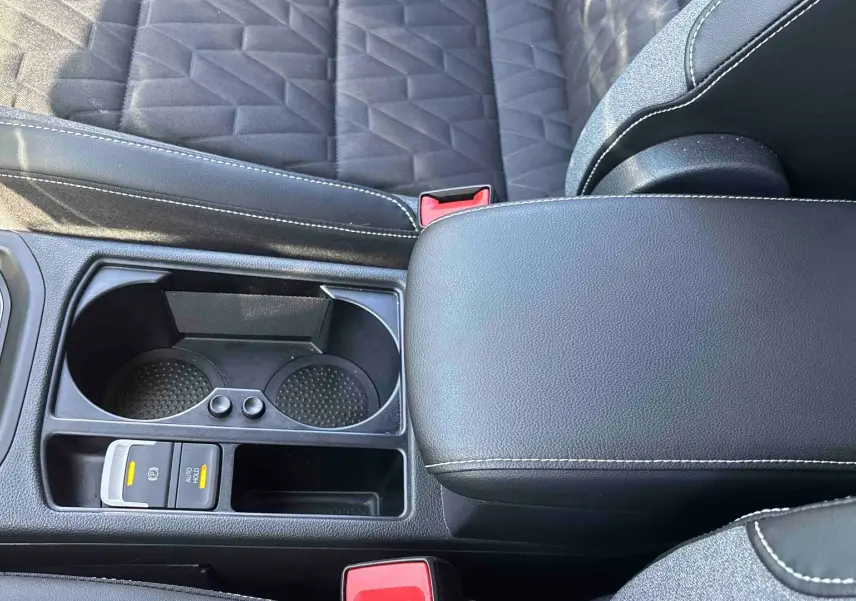 Vue rapprochée de la console centrale noire du Volkswagen Touran 2025 avec accoudoir et porte-gobelets.