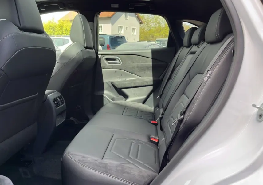 Vue côté droit de l’habitacle arrière du Nissan Qashqai blanc nacré, avec sellerie cuir alcantara noire et vitres surteintées.
