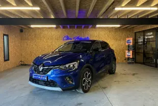 Renault Captur bleu 3/4 avant droit en intérieur, avec calandre chromée et jantes distinctives.
