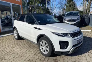 Vue 3/4 avant gauche d'un Range Rover Evoque blanc avec toit noir, garé devant un showroom.