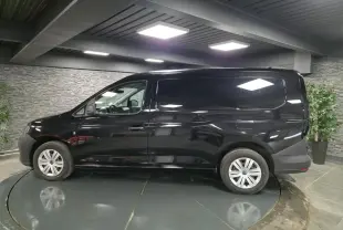 Vue de profil côté gauche d'un Volkswagen Caddy Cargo noir avec jantes acier et portes tôlées en intérieur showroom.