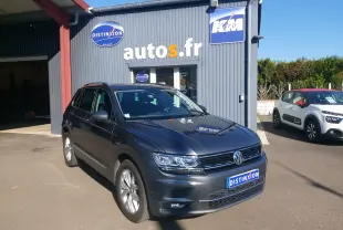 Volkswagen Tiguan gris 3/4 avant droit, avec phares LED et calandre noire, stationné devant un garage autos.fr.