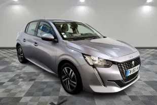 Peugeot 208 gris clair vue 3/4 avant droit, avec calandre noire et jantes alliage 16 pouces diamantées.