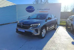 Renault Austral gris schiste en 3/4 avant droit, avec calandre distinctive et feux LED allumés, sur parking extérieur.