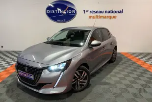 PEUGEOT 208 gris vue 3/4 avant droit, phares LED allumés, sur sol à damiers gris et orange en intérieur showroom.