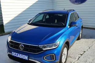 Volkswagen T-Roc bleu en 3/4 avant droit, avec calandre noire et feux LED, stationné devant un mur blanc.
