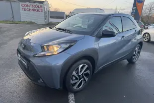 Toyota Aygo X bleu vue 3/4 avant droit avec phares allumés, roues alliage et carrosserie compacte cinq portes.