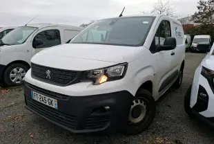 Fourgon Peugeot Partner blanc en 3/4 avant droit avec feu avant allumé sur parking extérieur.
