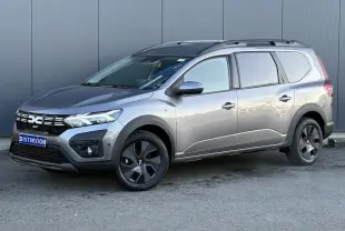 Vue 3/4 avant droite d'un Dacia Jogger gris schiste avec jantes noires et barres de toit longitudinales.