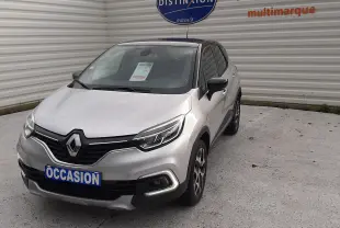 Renault Captur gris avec toit noir, vue 3/4 avant droit, stationné devant un mur blanc avec panneau Distinxion.