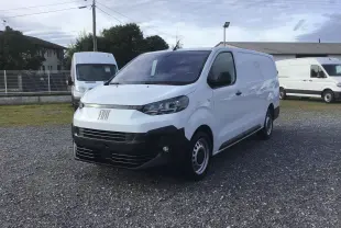 Fourgon FIAT Scudo blanc en 3/4 avant droit, avec pare-chocs noir et jantes acier, stationné sur un sol gravillonné.