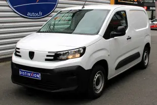 Peugeot Partner Fourgon blanc vue 3/4 avant droit avec calandre noire et feux allumés sur parking.