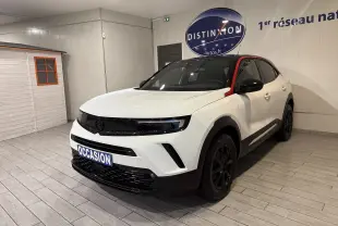 Opel Mokka blanc vue 3/4 avant droit avec toit noir et bande rouge distinctive sur montant avant.