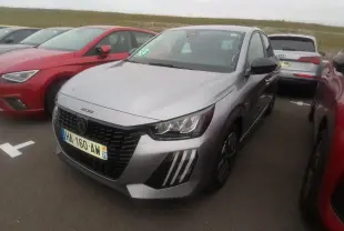 Peugeot 208 gris clair vue 3/4 avant droit, avec calandre noire et feux avant distinctifs en forme de griffes.