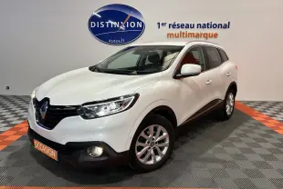Vue 3/4 avant droit d'un Renault Kadjar blanc avec feux allumés dans un showroom multimarque.