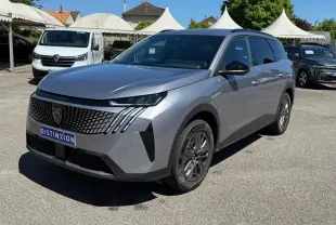 Peugeot 5008 gris clair en 3/4 avant droit, avec calandre distinctive et phares LED fins, sur parking extérieur.