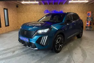 Peugeot 2008 hybride bleu en 3/4 avant droit dans un garage, avec calandre noire et feux LED distinctifs allumés.