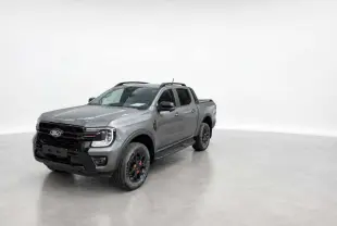Ford Ranger Wildtrak gris carbone en 3/4 avant droit, avec jantes noires et barres de toit visibles.