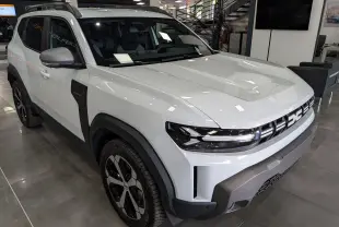 Vue 3/4 avant droite du Dacia Duster Hybrid-G blanc Glacier avec jantes bi-ton et protections noires contrastantes.