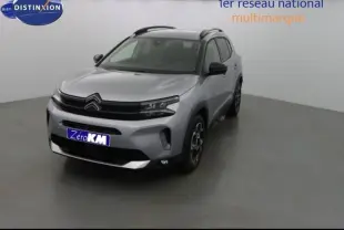 Citroën C5 Aircross gris acier vu en 3/4 avant droit, avec barres de toit et jantes alu distinctives.