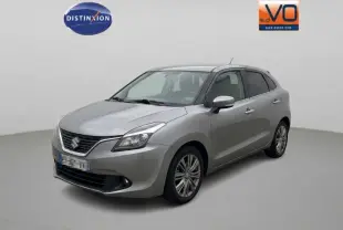 Suzuki Baleno gris clair vue 3/4 avant droit, jantes alliage 16 pouces et vitres surteintées visibles.