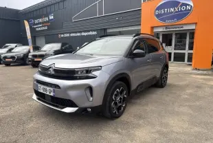 Citroën C5 Aircross gris en 3/4 avant droit, avec jantes alliage et barres de toit noires, devant un concessionnaire.