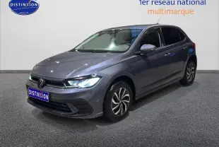 Volkswagen Polo gris cendre vue 3/4 avant droit avec phares allumés sur fond neutre intérieur.