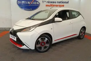Vue 3/4 avant droite d'une Toyota Aygo blanche avec détails noirs et rouges, jantes stylisées et phares ellipsoïdaux.