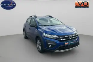Dacia Sandero Stepway bleu foncé vue 3/4 avant droit avec barres de toit et feux allumés sur fond neutre.