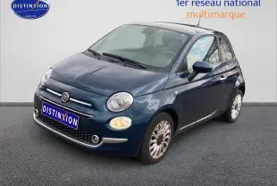 Vue 3/4 avant droite d'une Fiat 500 bleu foncé avec jantes alu et phares allumés sur fond neutre.