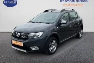 Dacia Sandero Stepway gris foncé vue 3/4 avant droit avec barres de toit et jantes alliage.