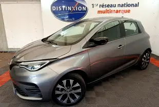 Renault ZOE gris clair en 3/4 avant droit, avec jantes alliage et phares LED, en intérieur showroom.