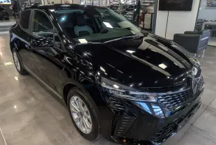 Vue 3/4 avant droite d'une Renault Clio V noire 2025 en intérieur, avec calandre et phares LED distinctifs.