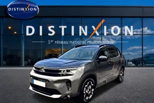 Citroën C5 Aircross gris platinium en 3/4 avant droit, avec jantes alu et barres de toit visibles devant showroom Distinxion.