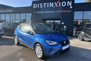 Vue 3/4 avant d'un SEAT Arona bleu saphir avec toit noir, stationné devant un bâtiment Distinxion.