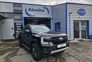 Ford Ranger Double Cabine noir en 3/4 avant droit, avec calandre imposante et marchepieds visibles devant un garage.