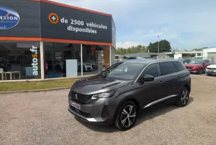 Peugeot 5008 gris métallisé vue 3/4 avant droit avec jantes bi-ton et calandre GT devant un concessionnaire.