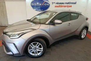 Vue 3/4 avant droit d’un Toyota C-HR 2.0 Hybride gris clair, avec jantes alliage et détails hybrides visibles sur l’aile.