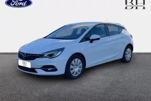 Opel Astra blanc glacier vue 3/4 avant droit, avec enjoliveurs et phares halogènes visibles.