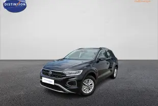 Volkswagen T-Roc noir vue 3/4 avant droit, stationné devant un bâtiment moderne de concession automobile.