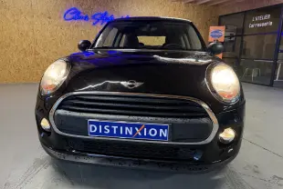 Vue avant d'une MINI noire 1.5i 75CV ONE de 2018 avec phares et antibrouillards allumés en intérieur.