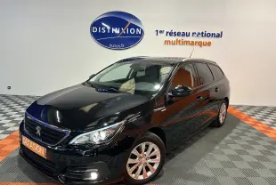 Peugeot 308 SW noire vue en 3/4 avant droit, avec jantes alliage et feux allumés dans un showroom.