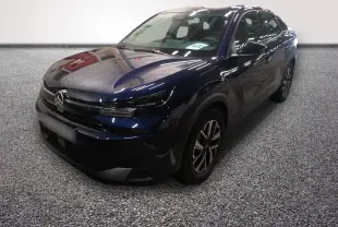Citroën C4 hybride bleu en 3/4 avant droit, avec calandre noire et phares LED fins, sur sol gris texturé.