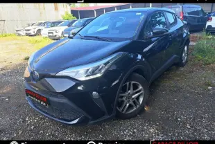 Vue 3/4 avant d'une Toyota C-HR 1.8 Hybride noire avec jantes alliage, garée sur un sol gravillonné.